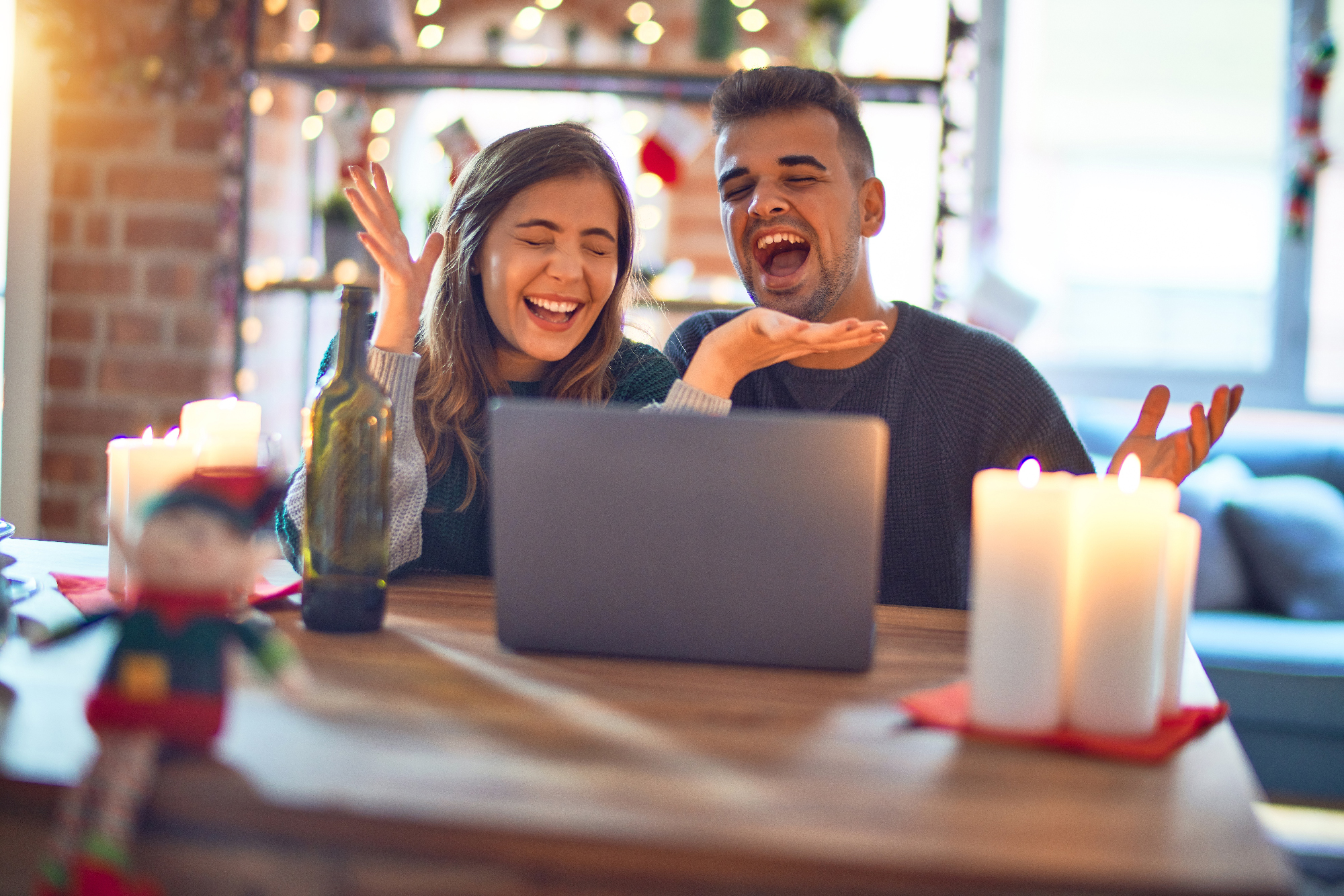 Young beautiful couple sitting using laptop around christmas decoration at home celebrating mad and crazy for success with arms raised and closed eyes screaming excited. Winner concept